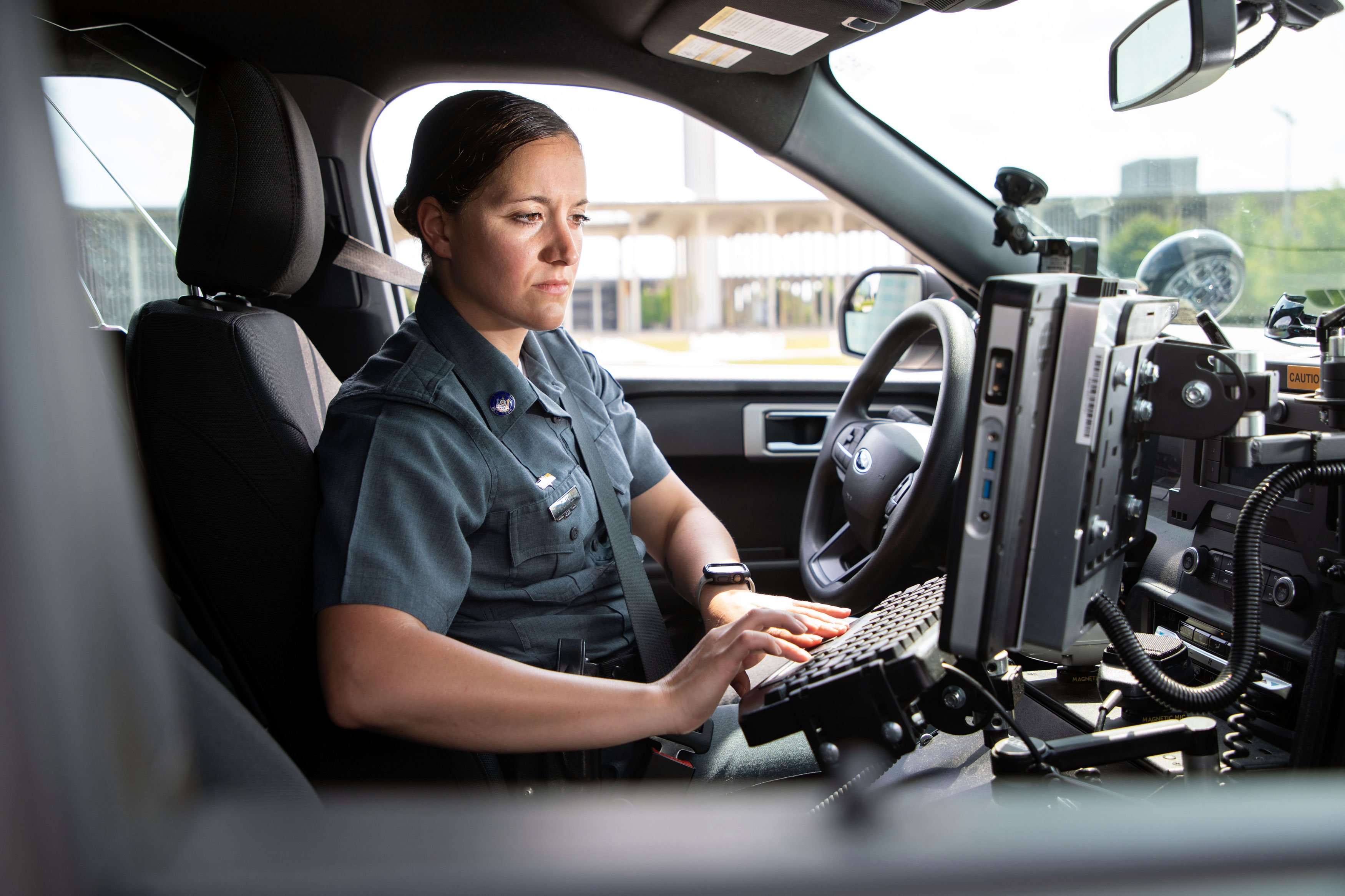 A University police officer looks at the computer screen inside her patrol car while typing on the keyboard.