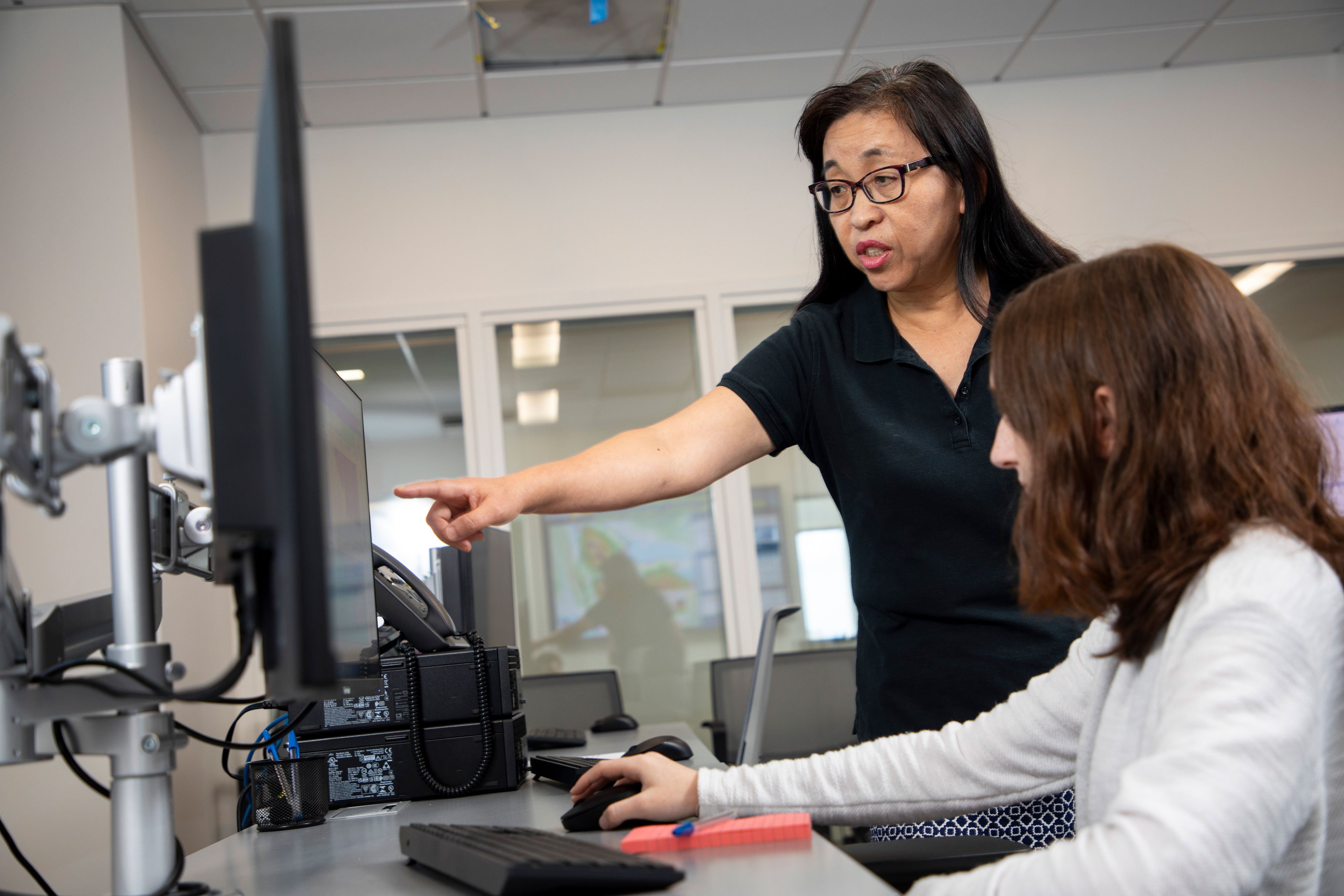 An instructor looks over a student's shoulder and points to their computer screen.