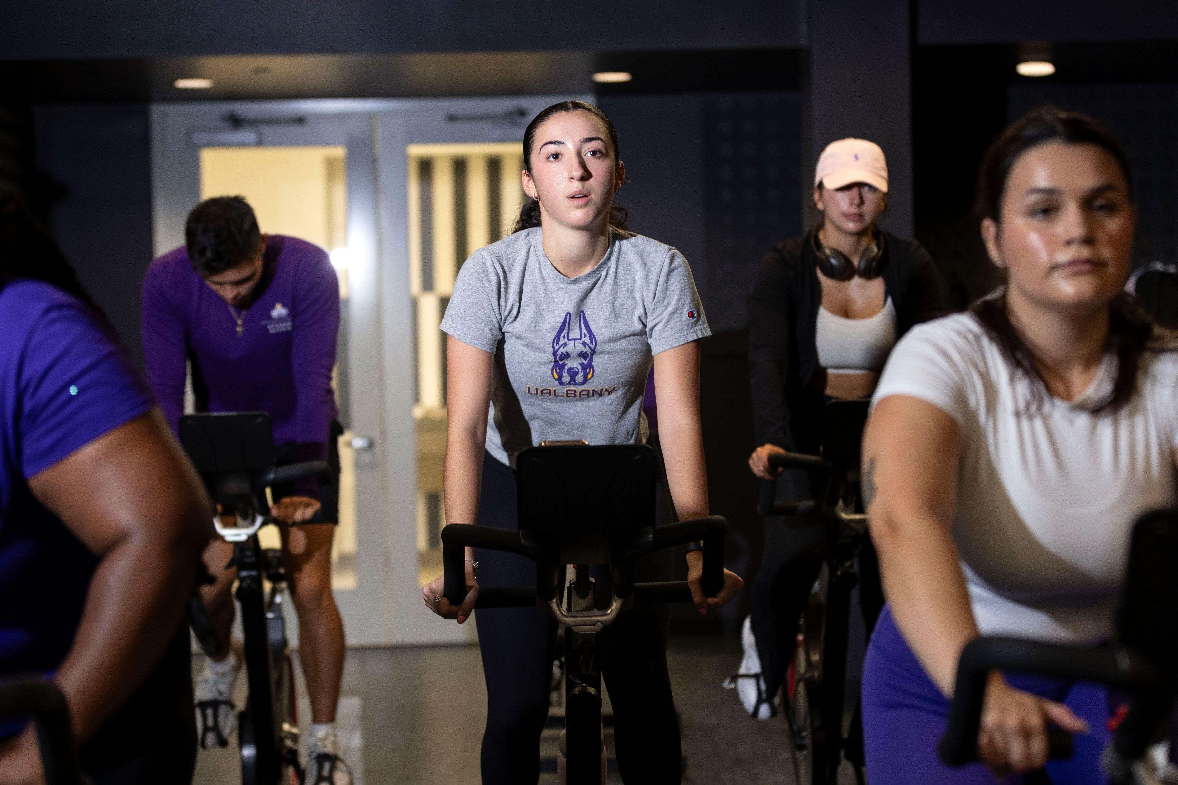 Students breath heavily and sweat as they participate in an indoor cycling class.