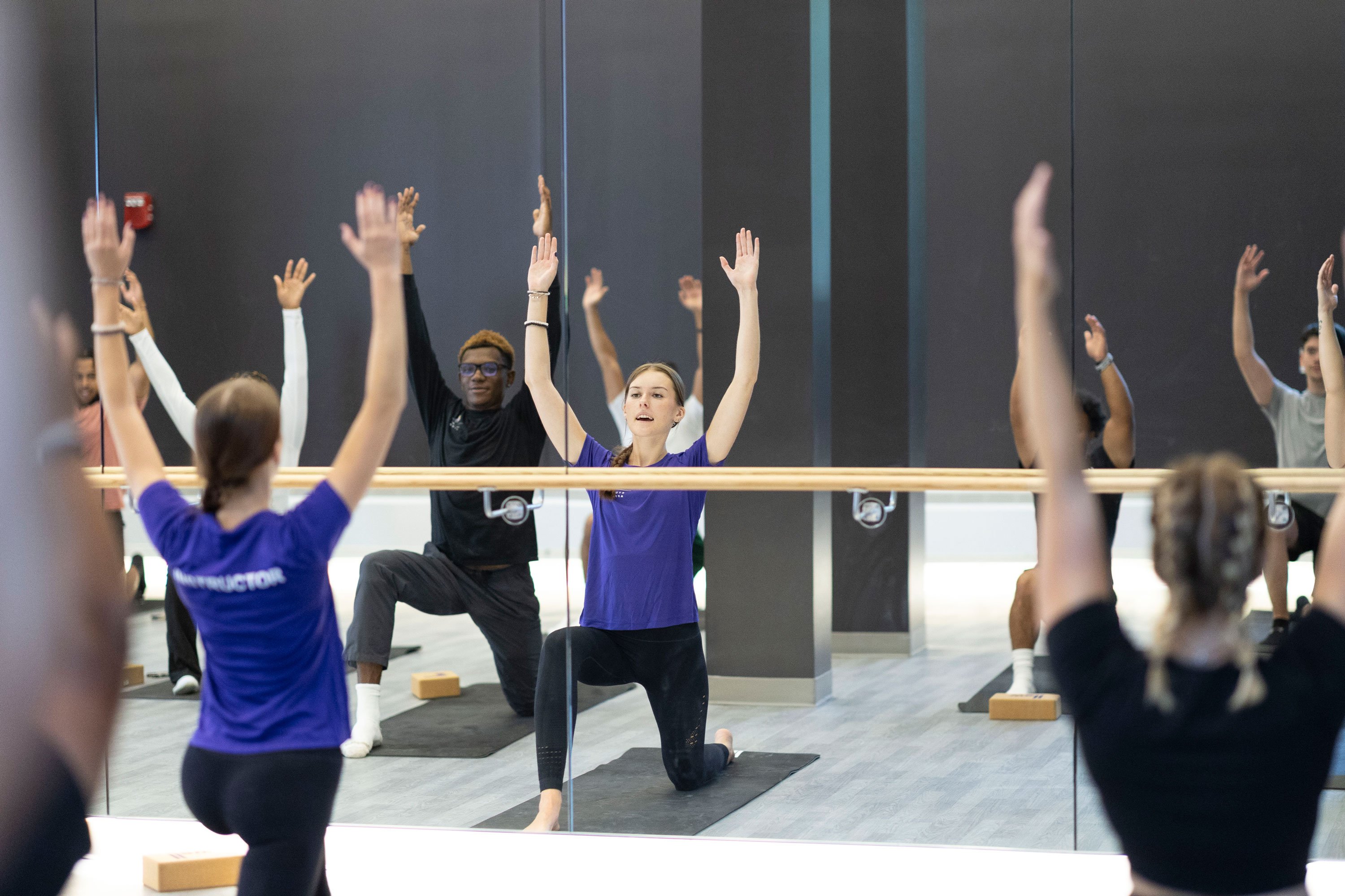 An instructor leads a yoga class in a group exercise room.