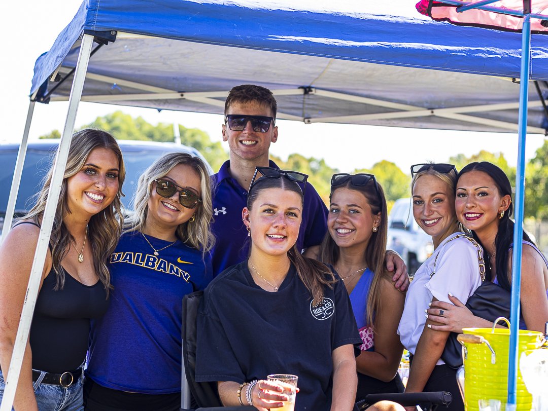 Seven people smile and pose for a group photo under a pop-up tent.