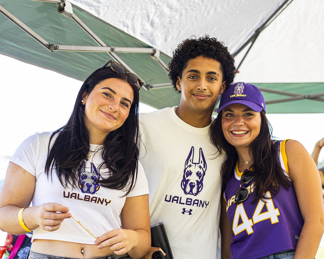 Three students wearing UAlbany gear smile and pose for a photo.