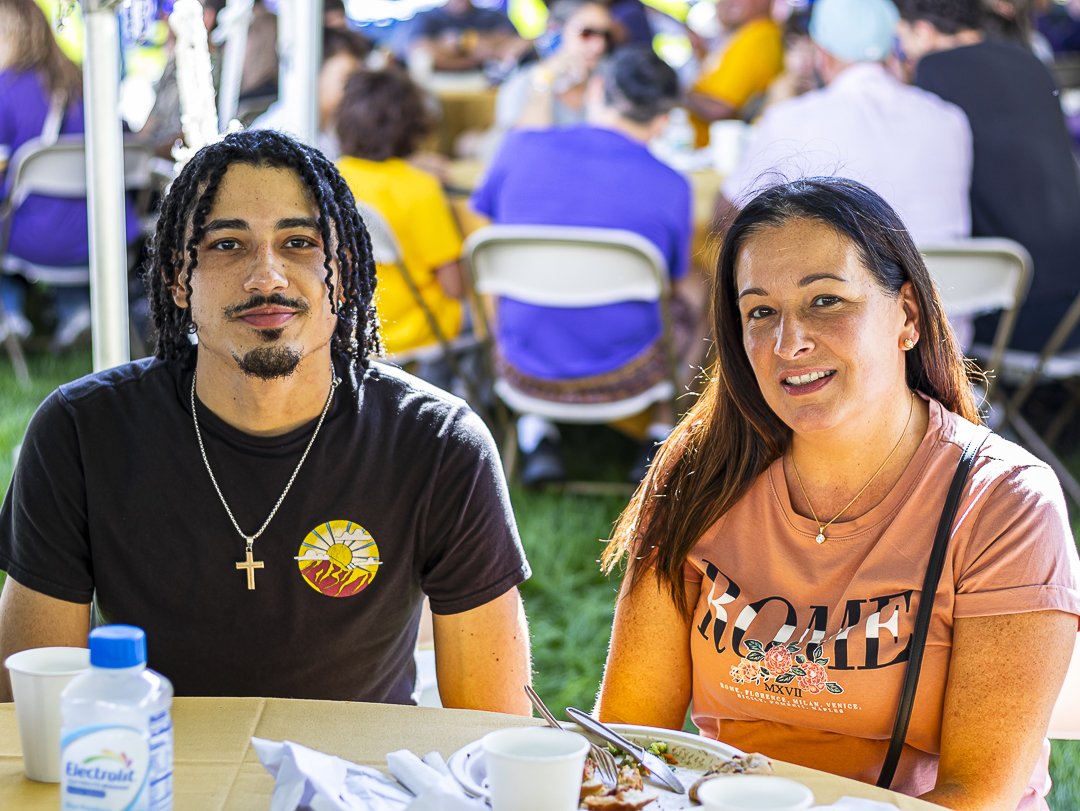 Two people sitting at a table with plates of food smile and pose for a photo.