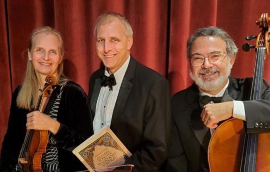 Three musicians sit smiling at the camera