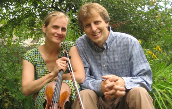 Two people pose for the camera surrounded by trees.