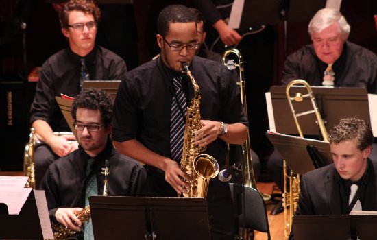 A performer plays a saxophone on stage surrounded by other musicians