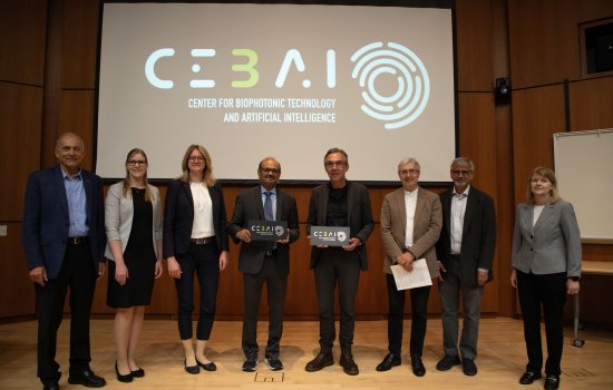 Leaders from UAlbany and the Leibniz Institute stand in front of a projection screen with the CEBAI logo on it.