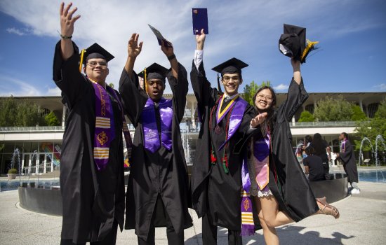 Four UAlbany students in their caps and gowns celebrate commencement