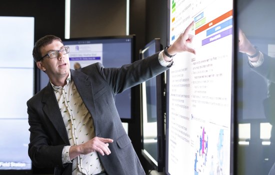 Nick Bassill points at a weather briefing on a projection screen inside UAlbany’s xCITE laboratory.