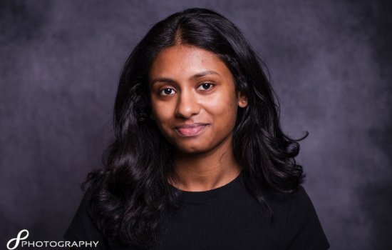A young woman with long hair wearing a black shirt, looking confidently at the camera.