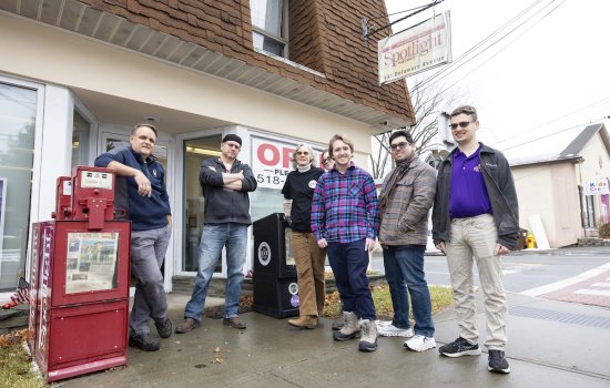 Seven people stand outside the Spotlight News office on an overcast day.