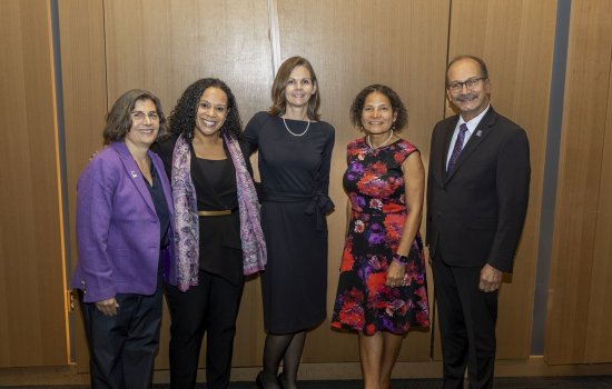 Four people dressed in business attire pose together for a group portrait in front of a wood-paneled wall.