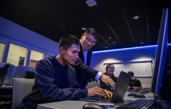 Alan Wang works with a student on his class project from the Cyber Range lab.