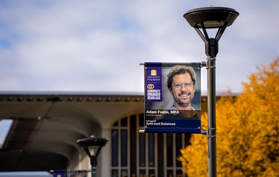A University at Albany campus streetlight displaying a Breathing Lights banner by Associate Professor Adam Frelin.