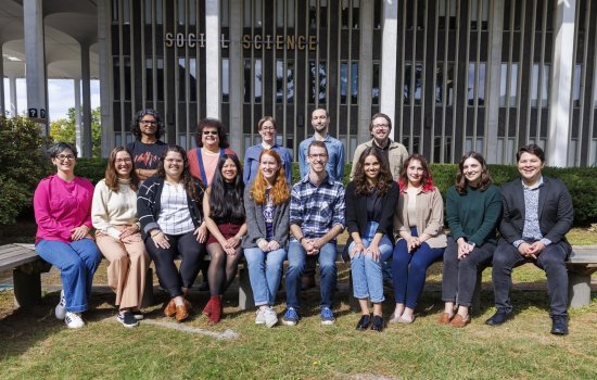 A diverse group of students stands in front of a building, smiling for a photo that highlights their unity and enthusiasm.