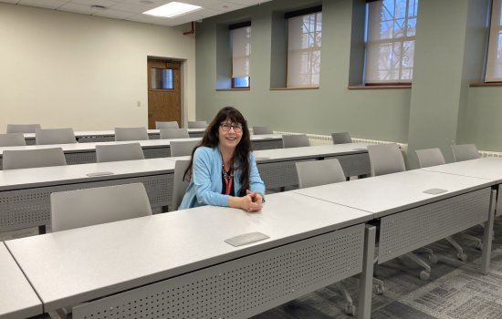 A smiling Mary Bayham sits in a row of seats inside a classroom.