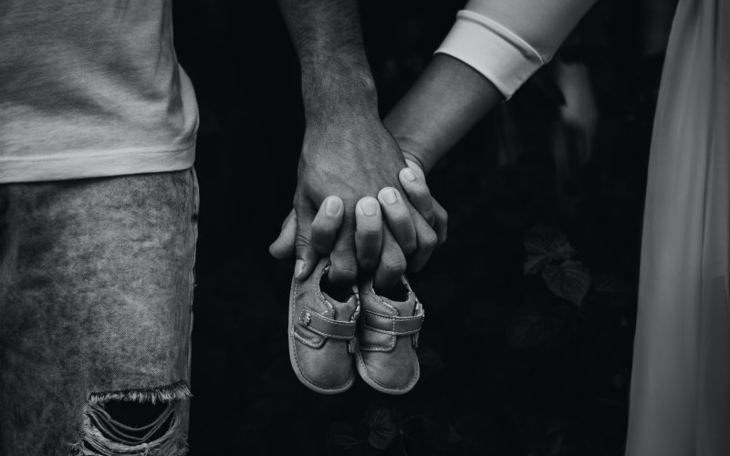 Two parents hold hands and a pair of baby shoes.