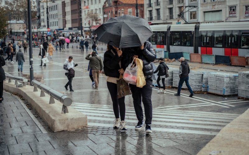 People walk through the rain holding umbrellas on a busy street.