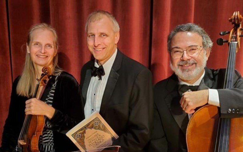 Three musicians sit smiling at the camera