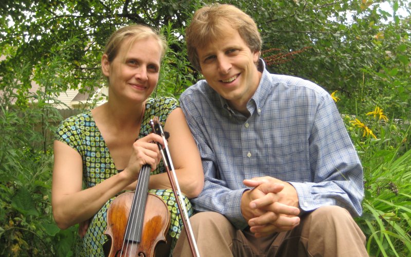 Two people pose for the camera surrounded by trees.