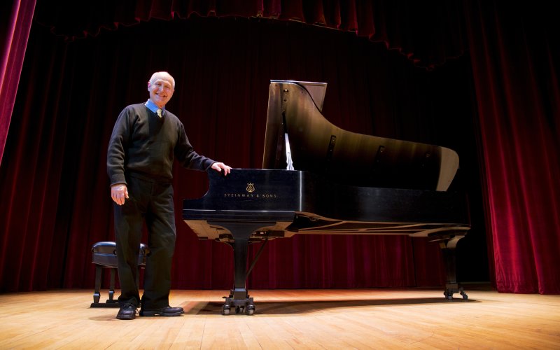 Man stands next to grand piano on stage