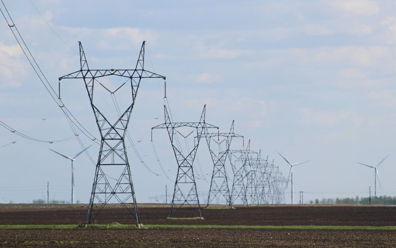 A row of power lines with windmills in the distance and blue skies above them.