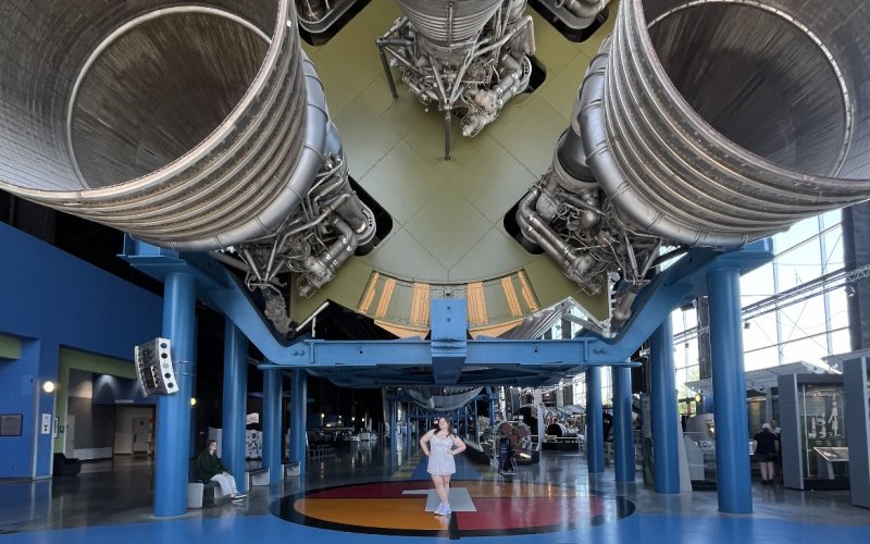 Abby Greco stands below the Saturn V rocket on display at the U.S. Space & Rocket Center in Huntsville, Alabama. She is spending the summer working at Space Camp, which is on the grounds of the center.