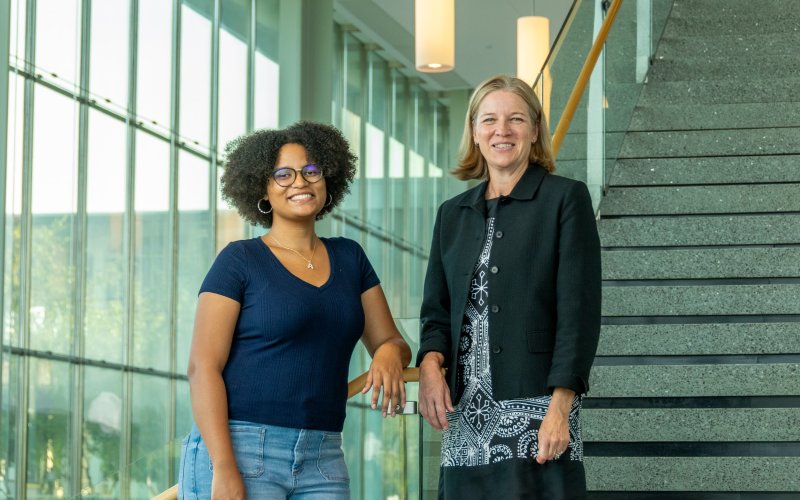 A UAlbany student and faculty member stand on the steps of the first floor of the Massry Center for Business.