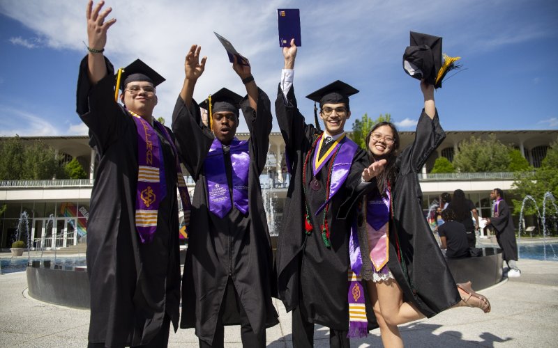 Four UAlbany students in their caps and gowns celebrate commencement