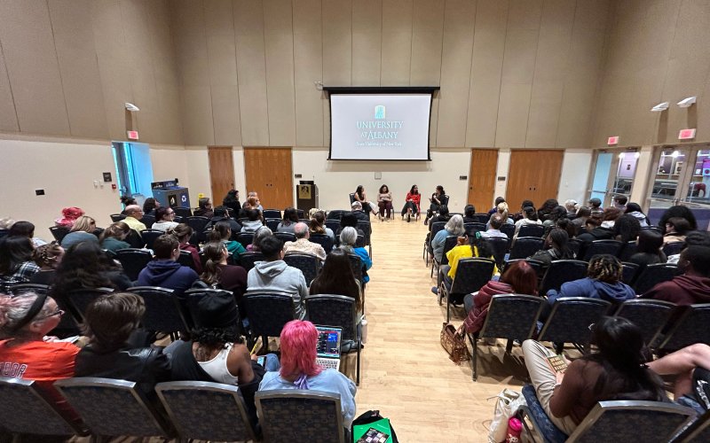 A room full of people listen to four panelists speak during a conversation and Q&A featuring authors Angie Cruz and Lilliam Rivera.