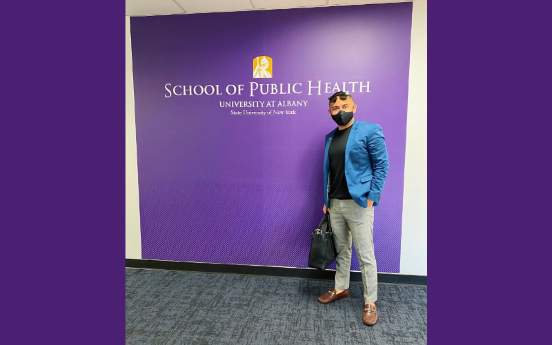 Man smiling at the camera, standing in from of the School of Public Health sign.