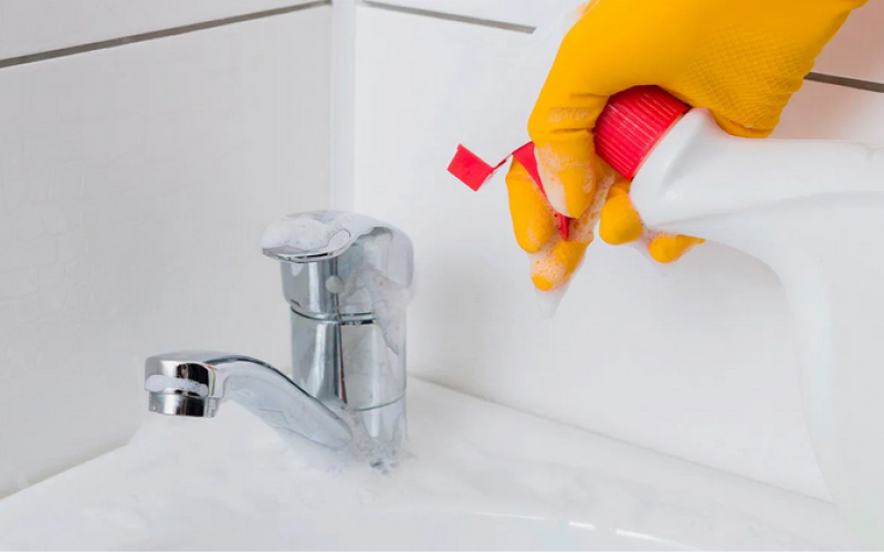 gloved hand spraying bleach on faucet