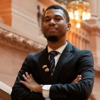 Nicholas poses arms crossed and in a suit in Albany capital building.