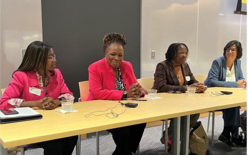 Four panelists smile while seated along a table.