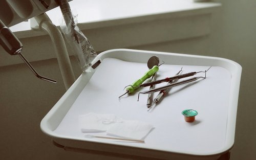 White plastic tray of dental implements including white gauze pads, various metal picks, and a small container of fluoride with a green metallic cap.