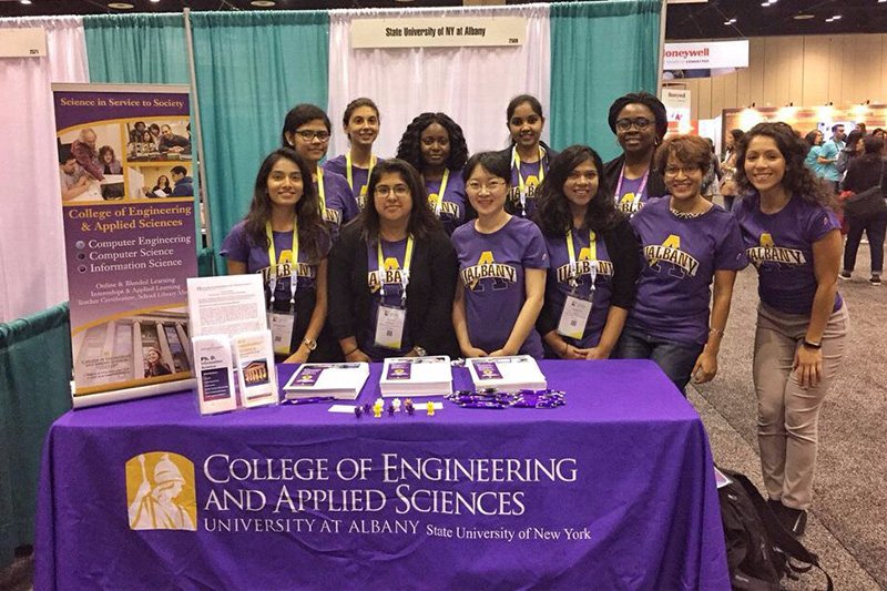 a group of 10 people standing at a university at albany college of engineering and applied sciences table