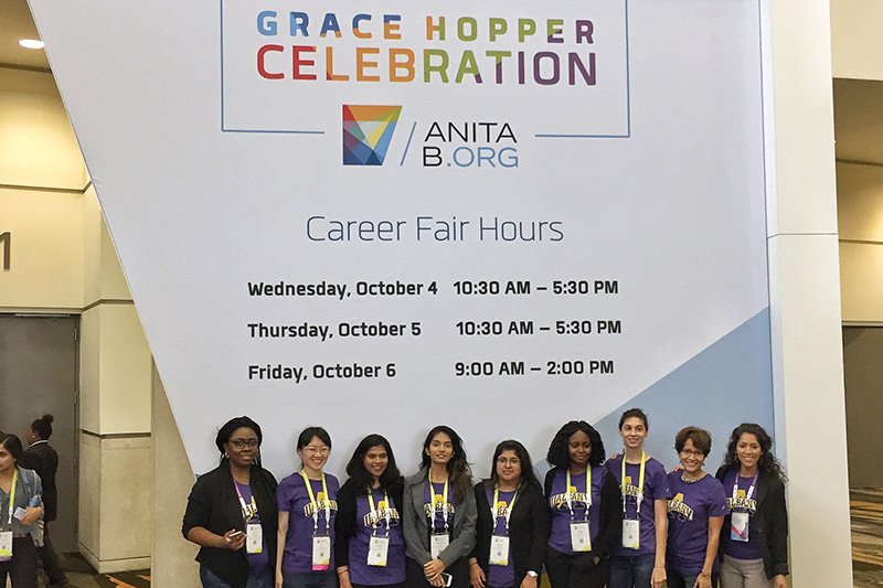 a group of 9 people standing in front of a grace hopper celebration sign