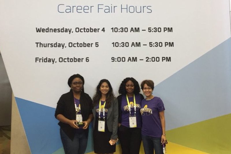 four people in front of a grace hopper celebration sign