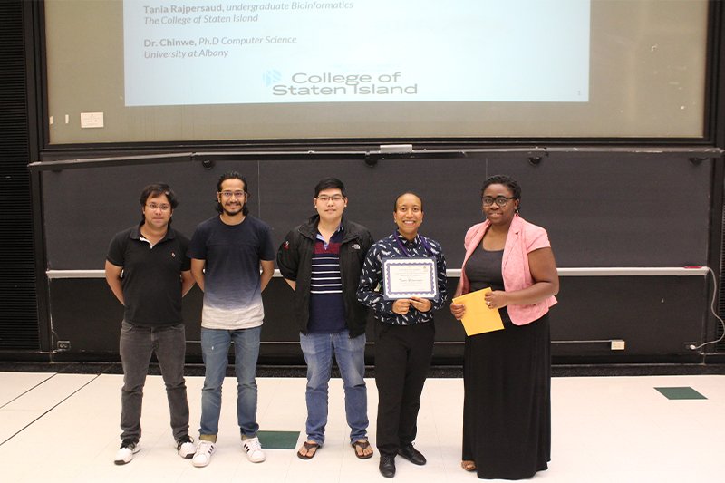 five people in front of a blackboard with one being presented a certificate of completion