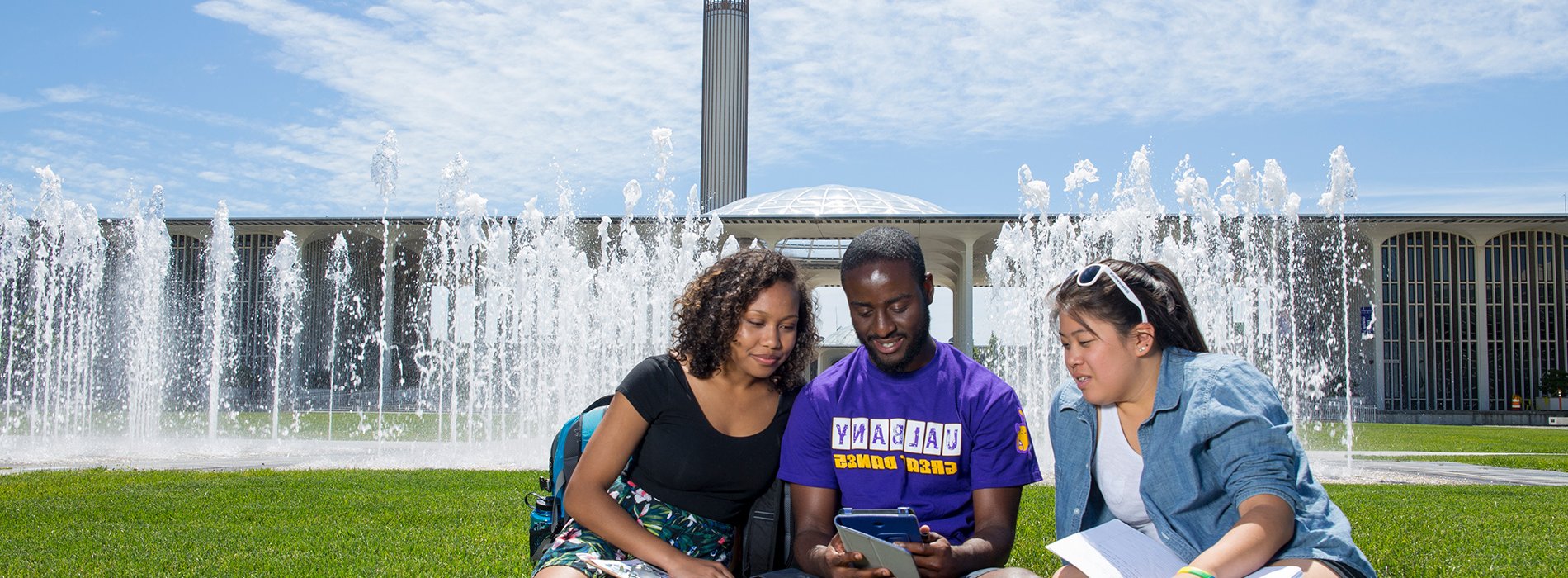 three students sitting by the entrance fountain