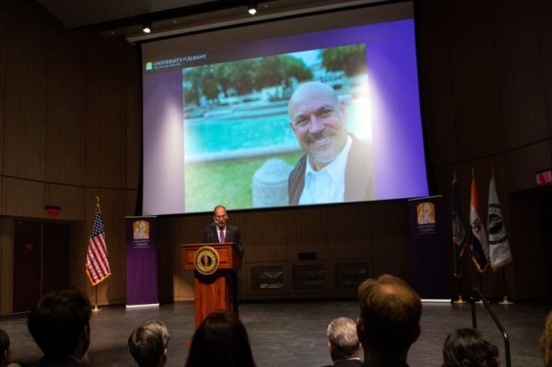 UAlbany President presenting ISHE director to a room full of people on a large projector