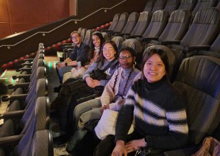Students sit and smile in a row of seats at the movie theater.