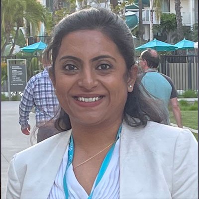 Kahini Sarkar stands outside smiling in a white blouse, white blazer and white bouse.