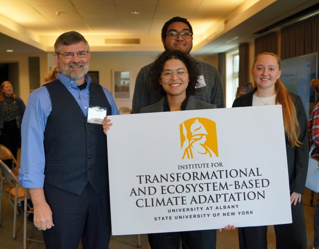 Four ITECA staff members pose for a photo while holding a sign with the institute's name and the UAlbany logo.