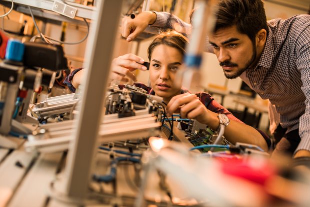 Two engineering students working on electrical component of a machine in laboratory.