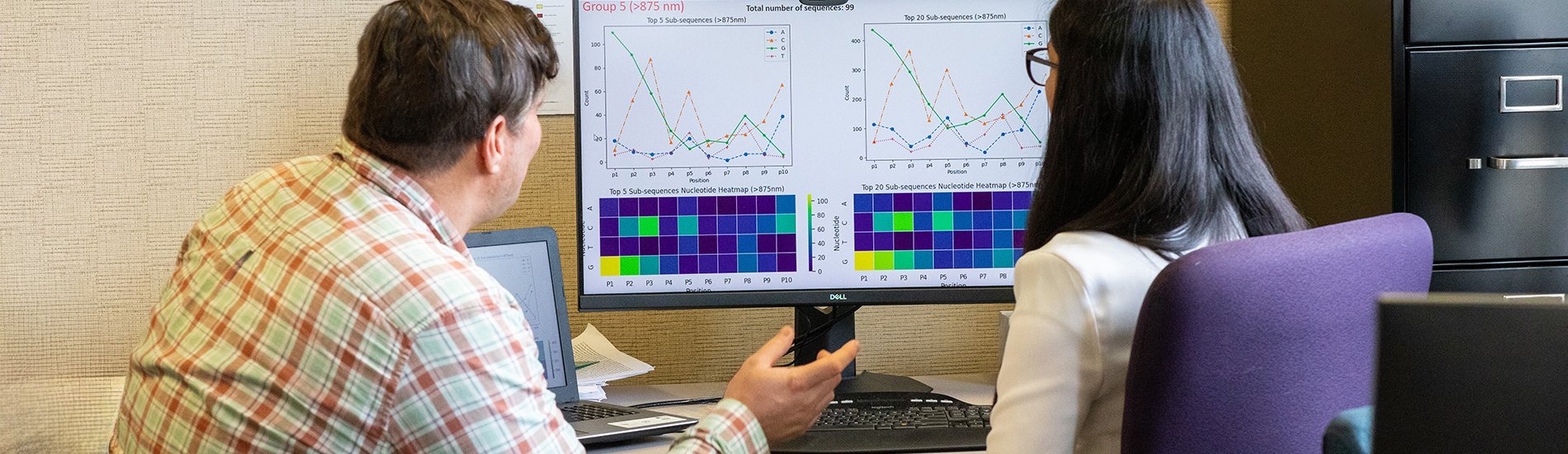 Two people looking at charts on a large computer monitor.