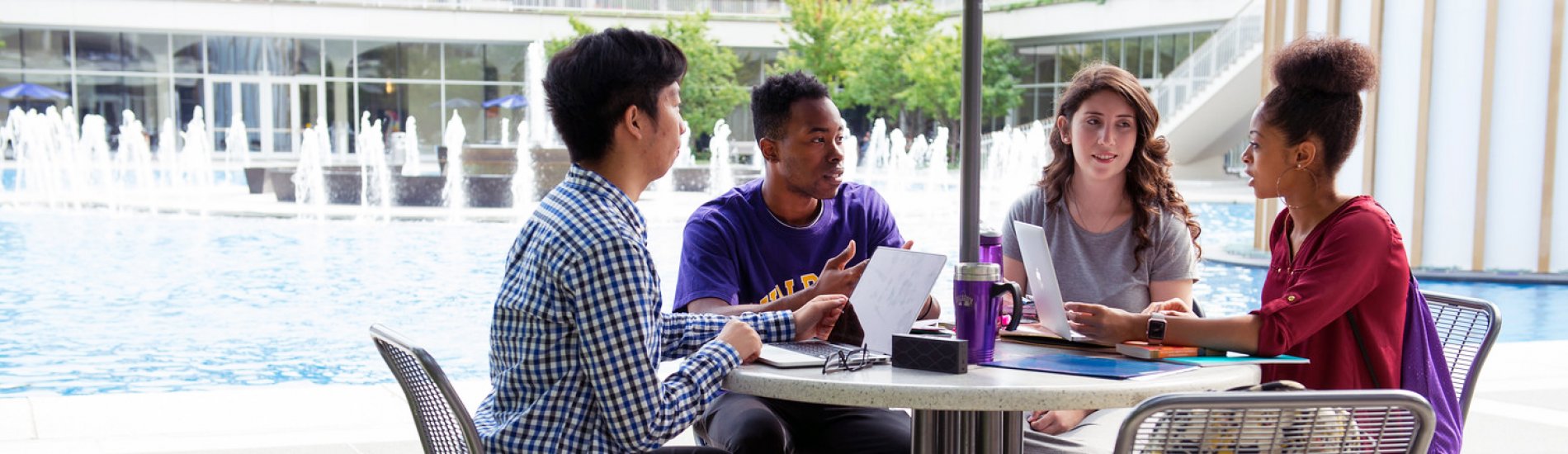 A group of four students studying at a table next to UAlbany's main fountain.