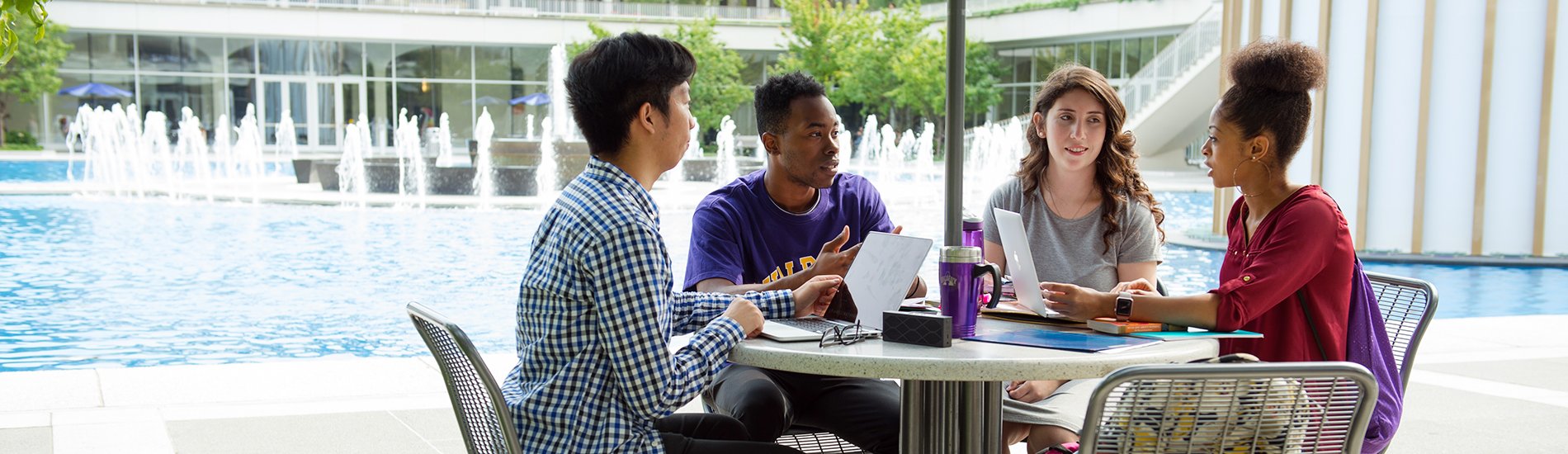 Four students having a discussion at a table next to the UAlbany main fountain.